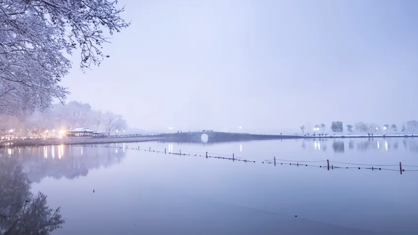 雪后断桥与岸边暖灯倒映湖面