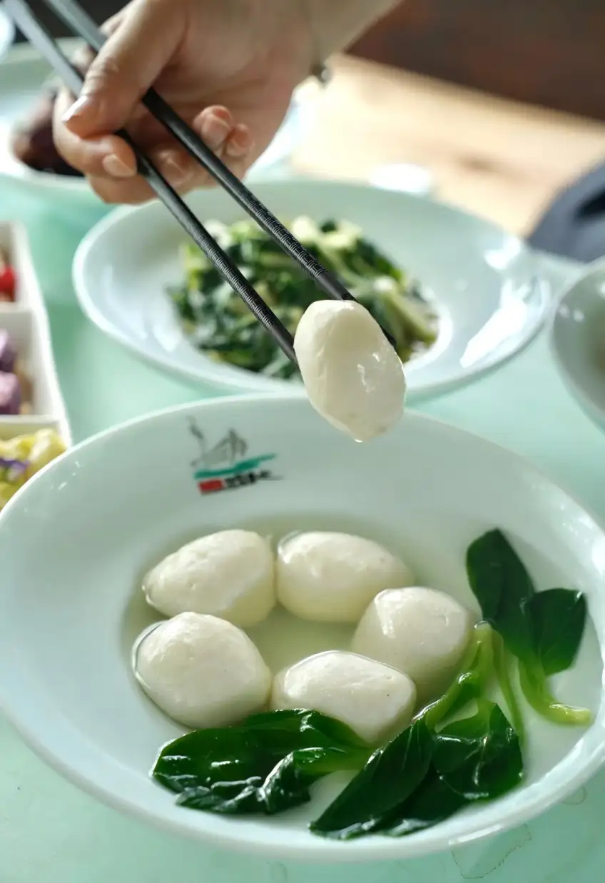 筷子夹起白鱼圆，碗中清汤青菜