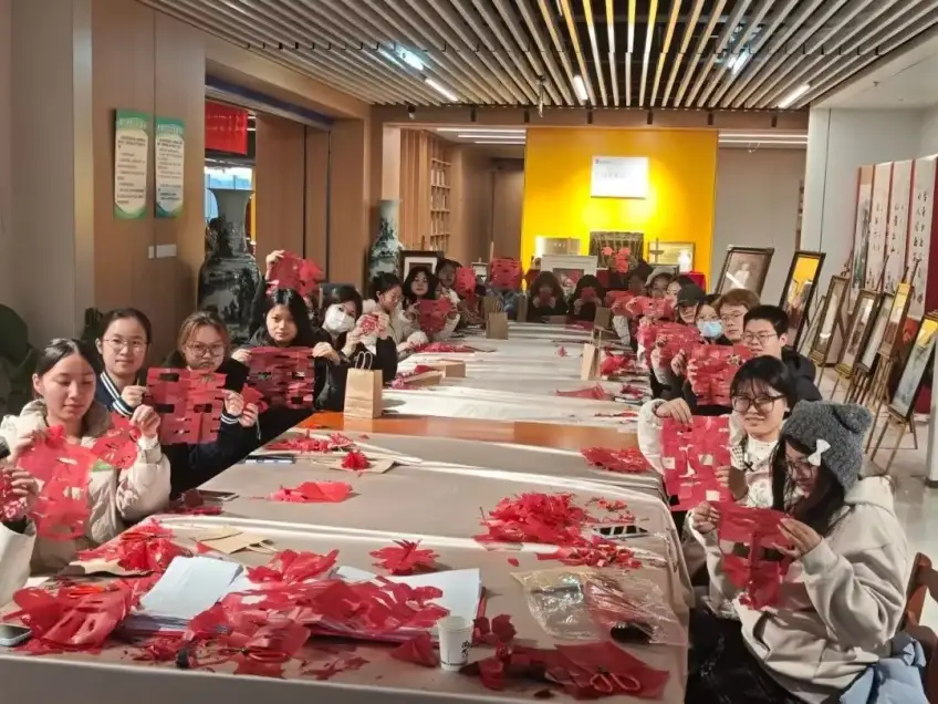 学员举红纸剪纸作品在工坊合影