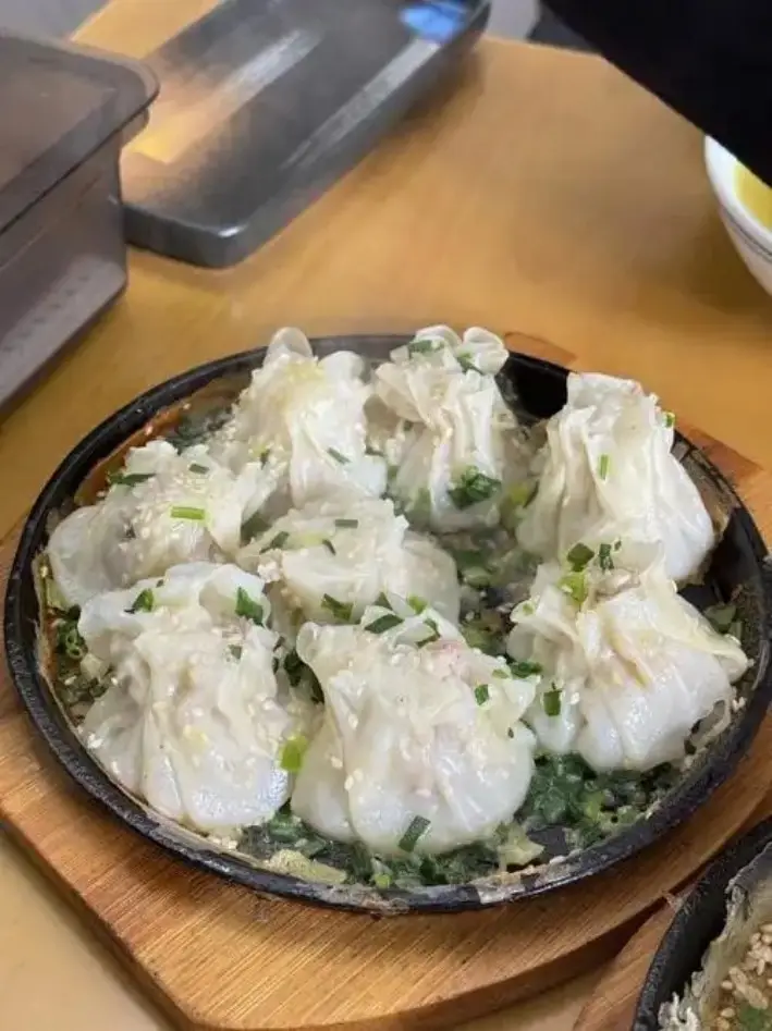 小铁锅中撒葱花芝麻的烧麦