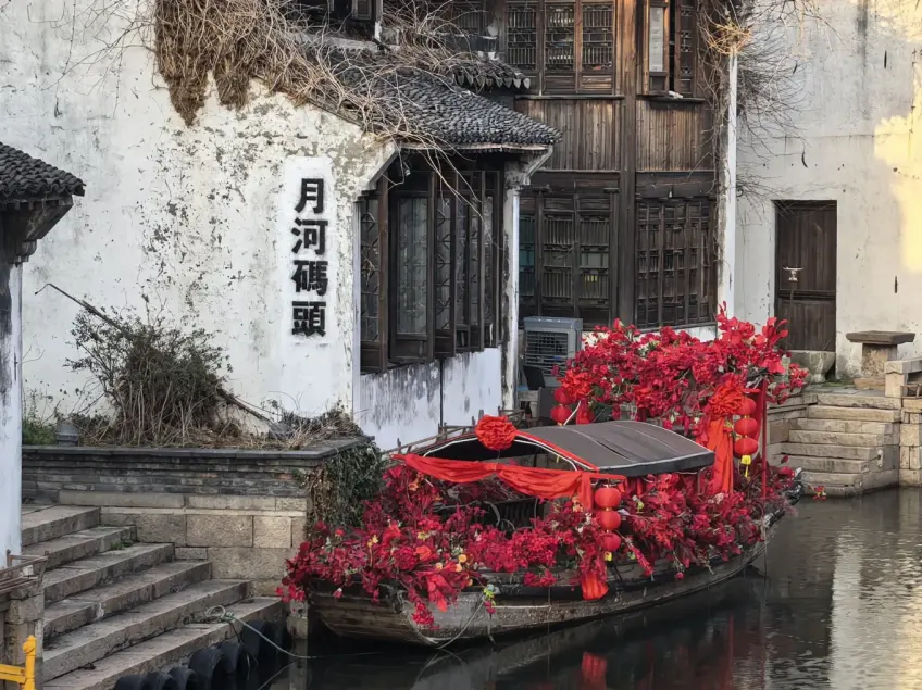 月河码头白墙与红花装饰乌篷船