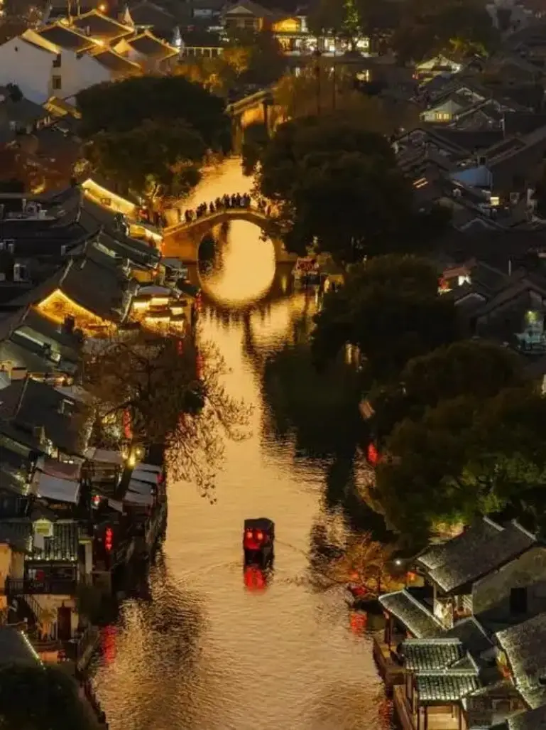 湖州水乡古镇夜景，拱桥与乌篷船灯火倒映水面