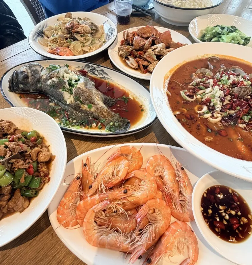 木桌擺滿白灼蝦清蒸魚與辣湯海鮮