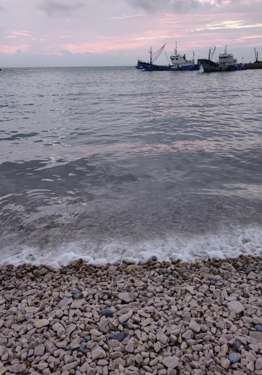 卵石灘浪花與遠方漁船晨昏