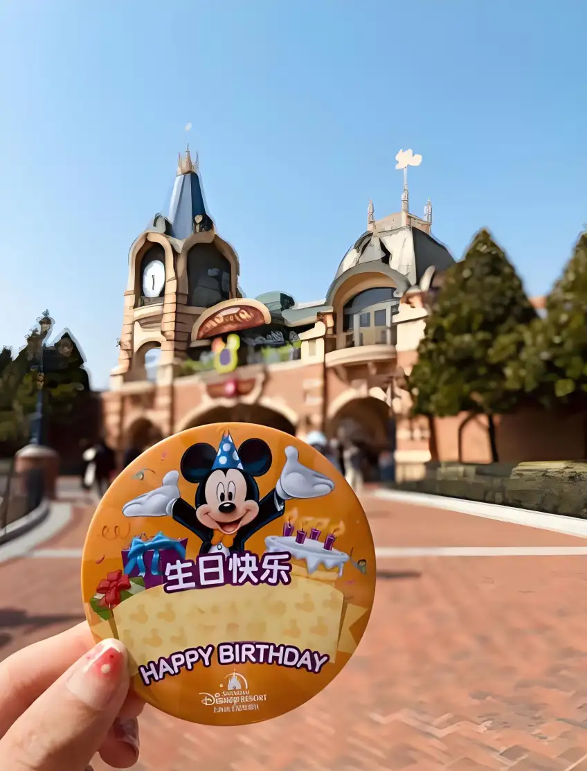 橙色生日快樂徽章與米奇派對帽在樂園入口前手持示意