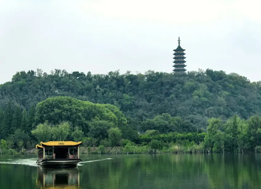 湖面畫舫與遠岸綠丘古塔同框