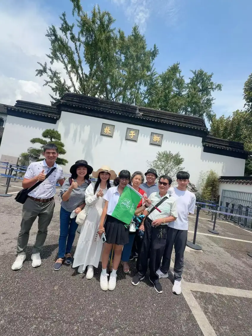 多代家庭在白牆黑瓦前合影舉綠旗